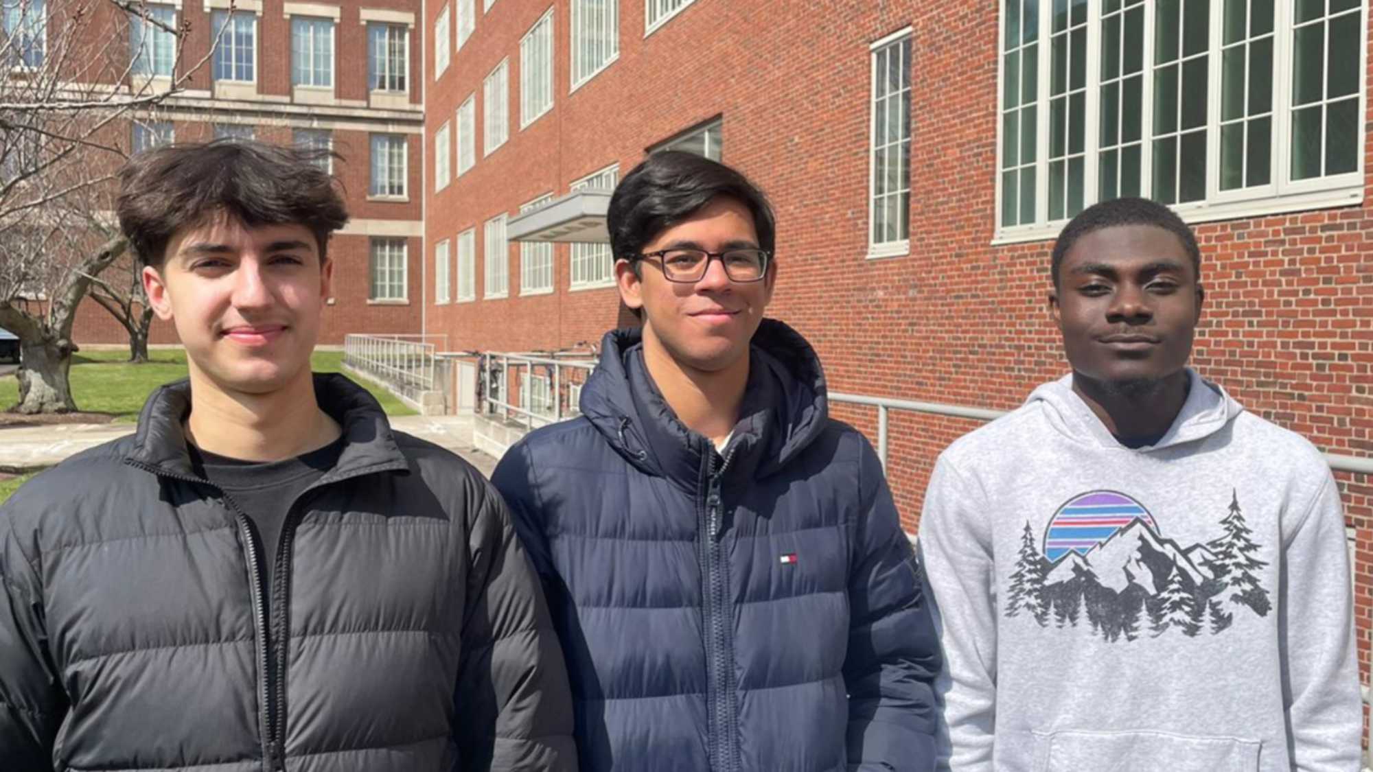 Three students in winter jackets and gear stand for a group photo on the River Campus.