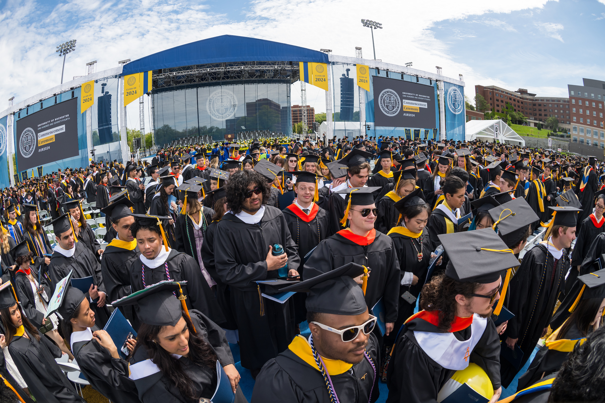 A sea of students in graduation regalia leave a stadium