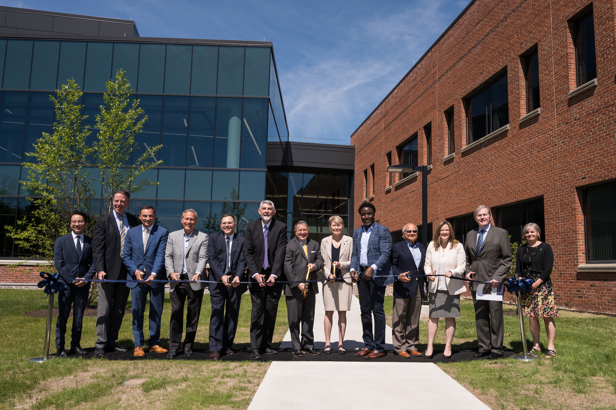 13 people lined up behind a blue ribbon, participating in a ribbon cutting ceremony
