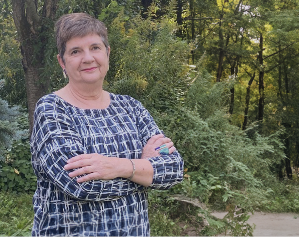 Janet Berlo crosses her arms in front of a background of trees.