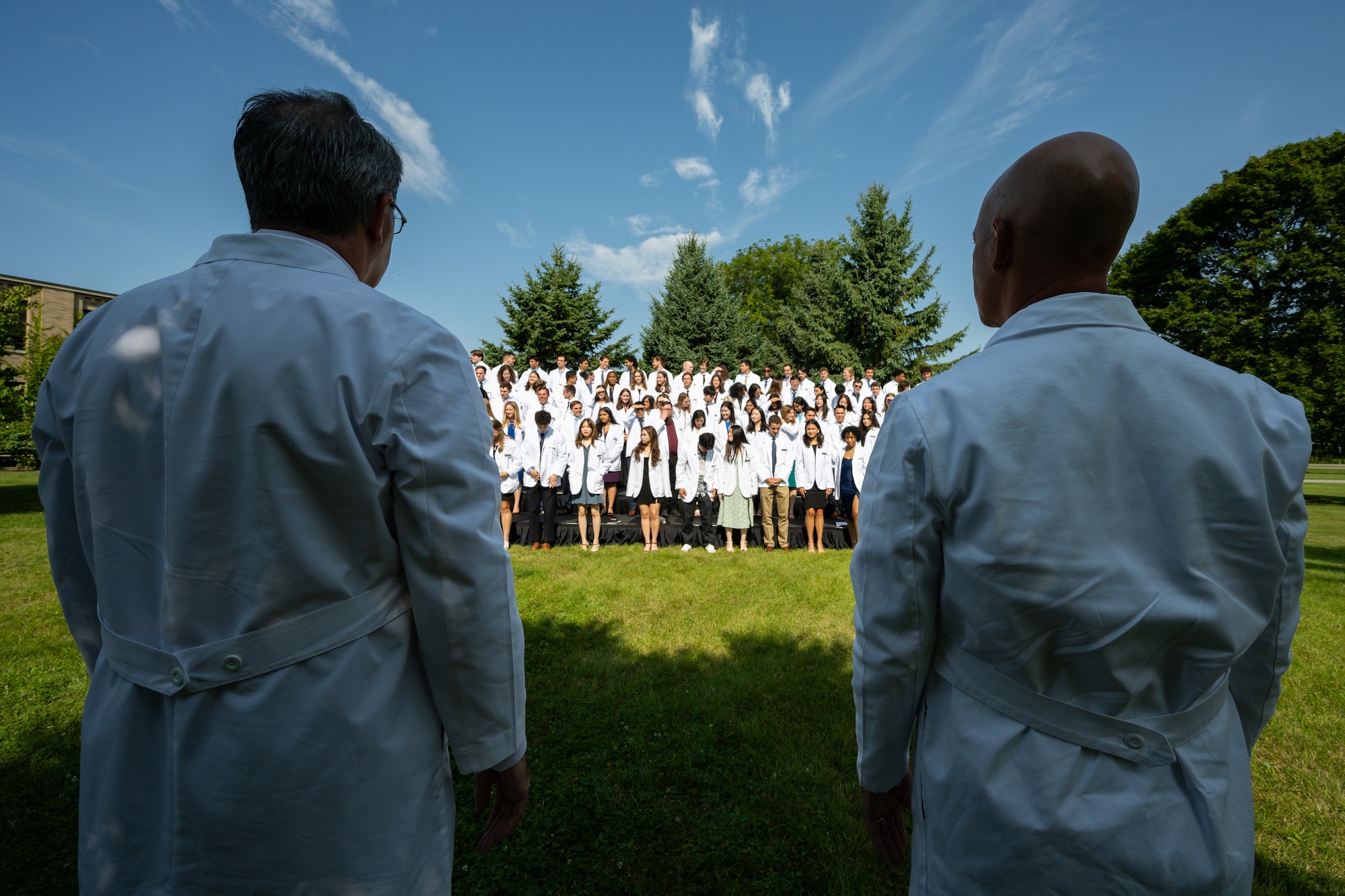 Two doctors watch on as medical students in white coats pose for a photo