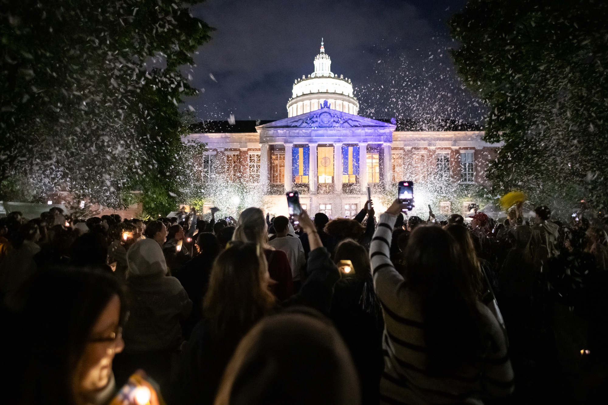 Students hold cell phones and lights during a candle light ceremony outside Rush Rhees Library