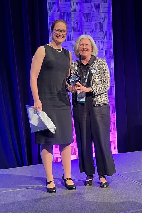Two women pose on stage with an award.