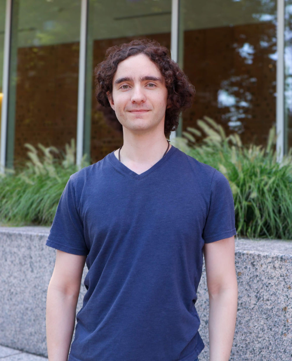 Alejandro Cruz Setzekorn faces and smiles at the camera outside of Wegmans Hall at the University of Rochester.l