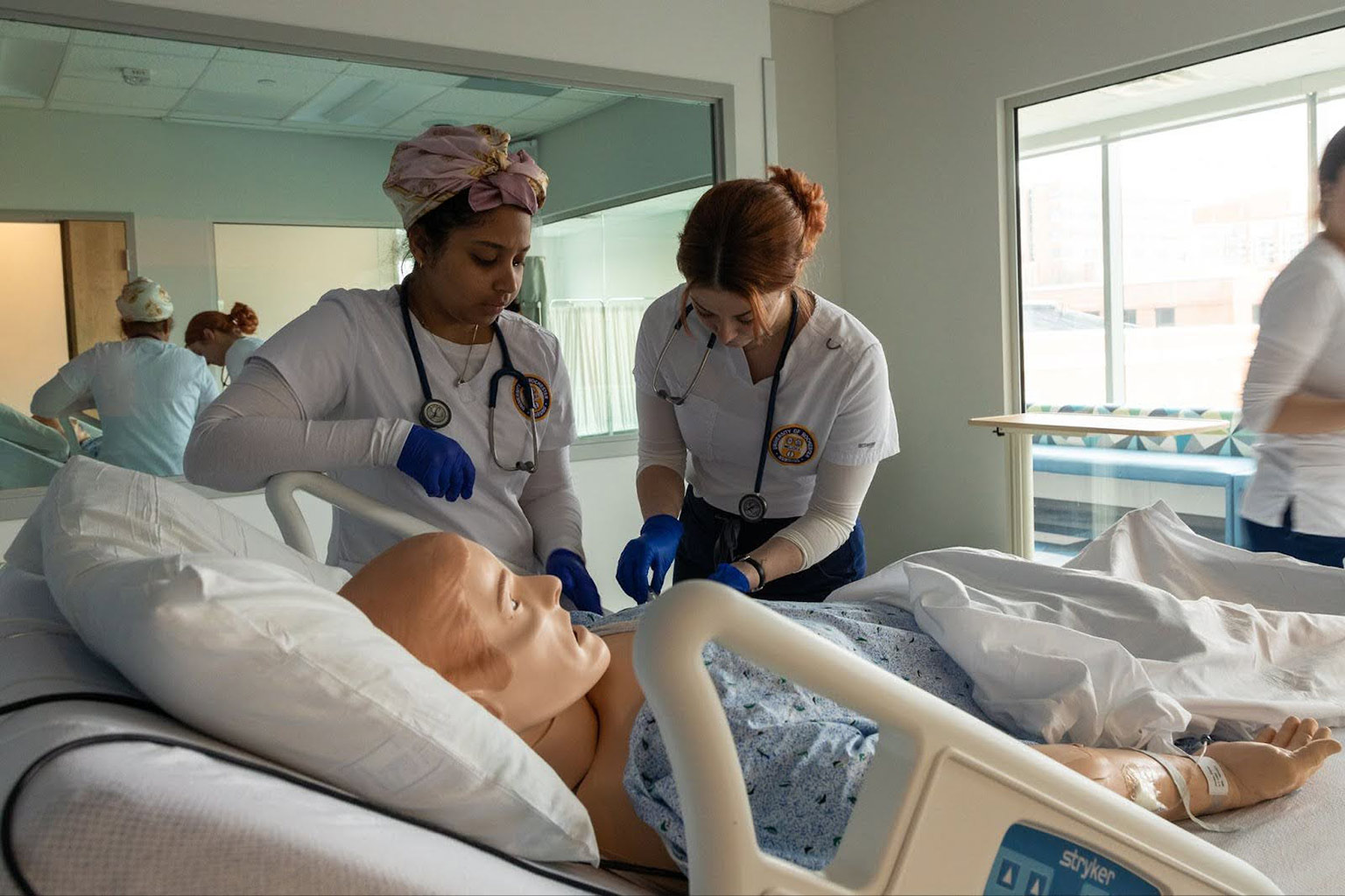 two nurses examining a mannequin lying in a hospital bed.