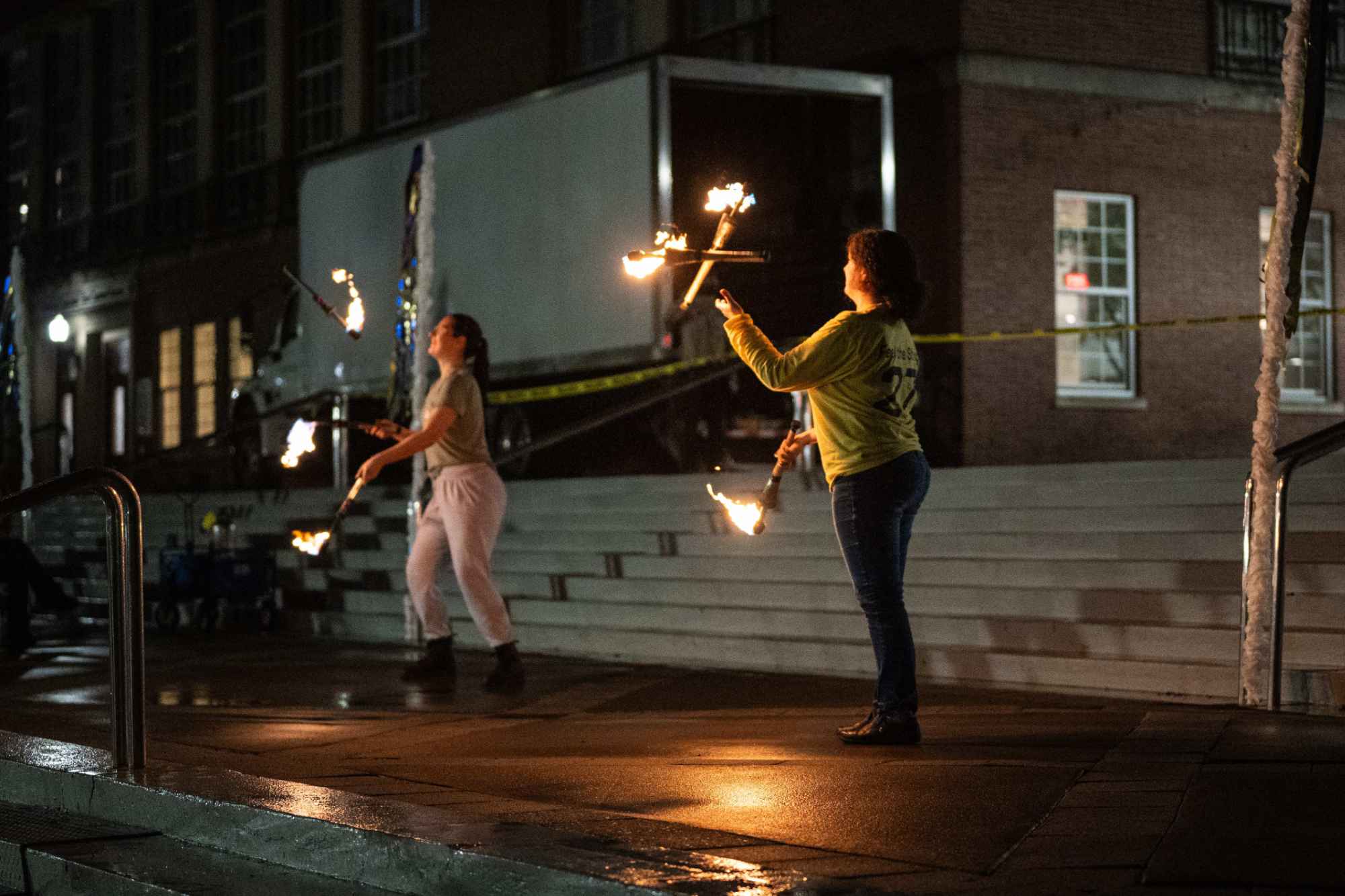 Two people juggling items on fire at night.