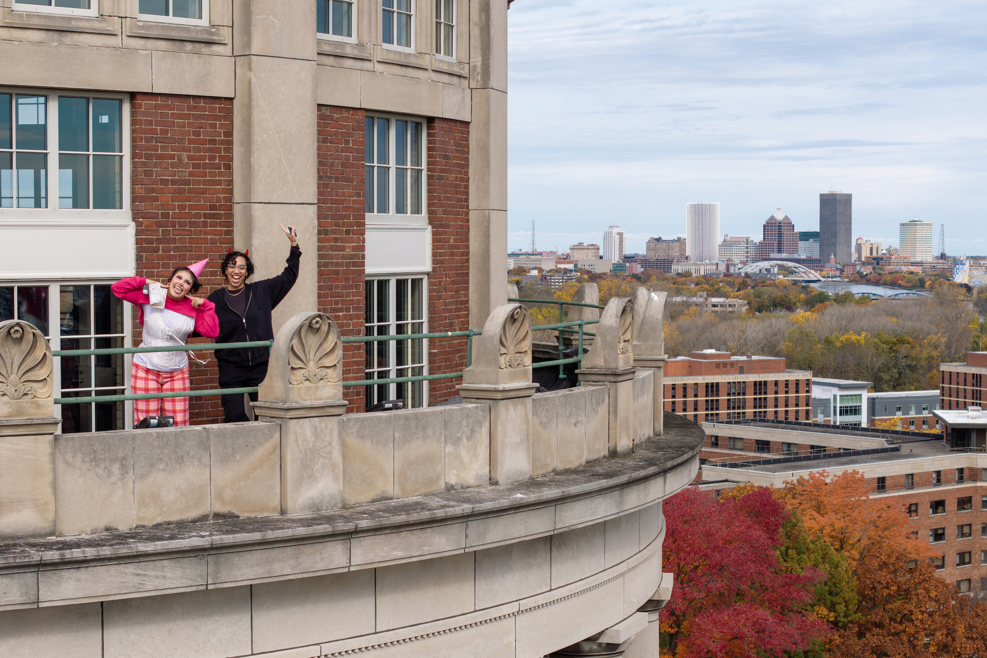 Two people in Halloween costumes wave from the Rush Rhees Library tower