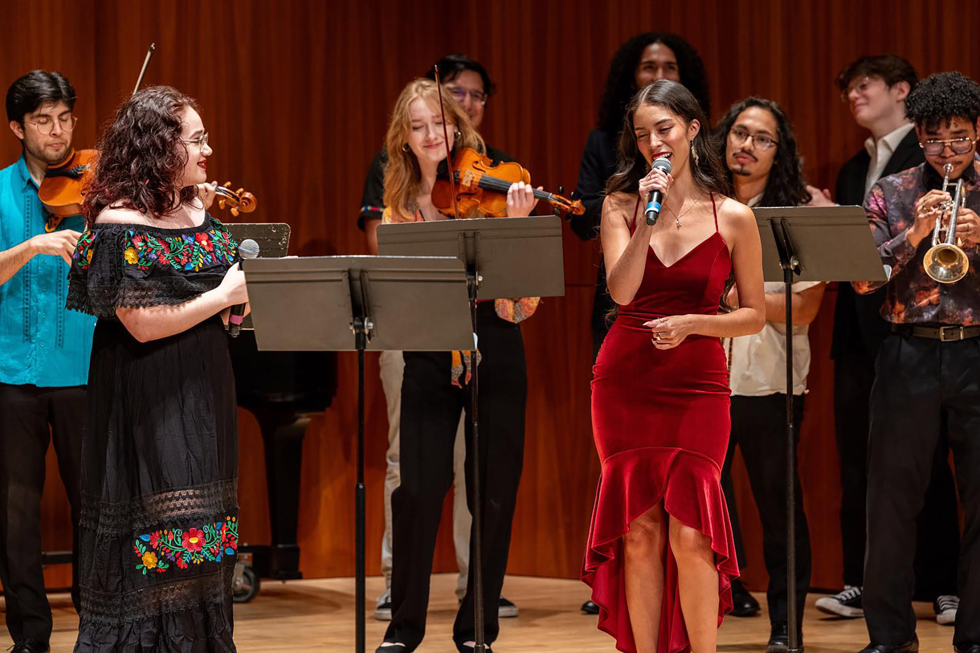 Nichole Waligóra singing on stage, surrounded by other musicians playing violins, trumpets, and other instruments.