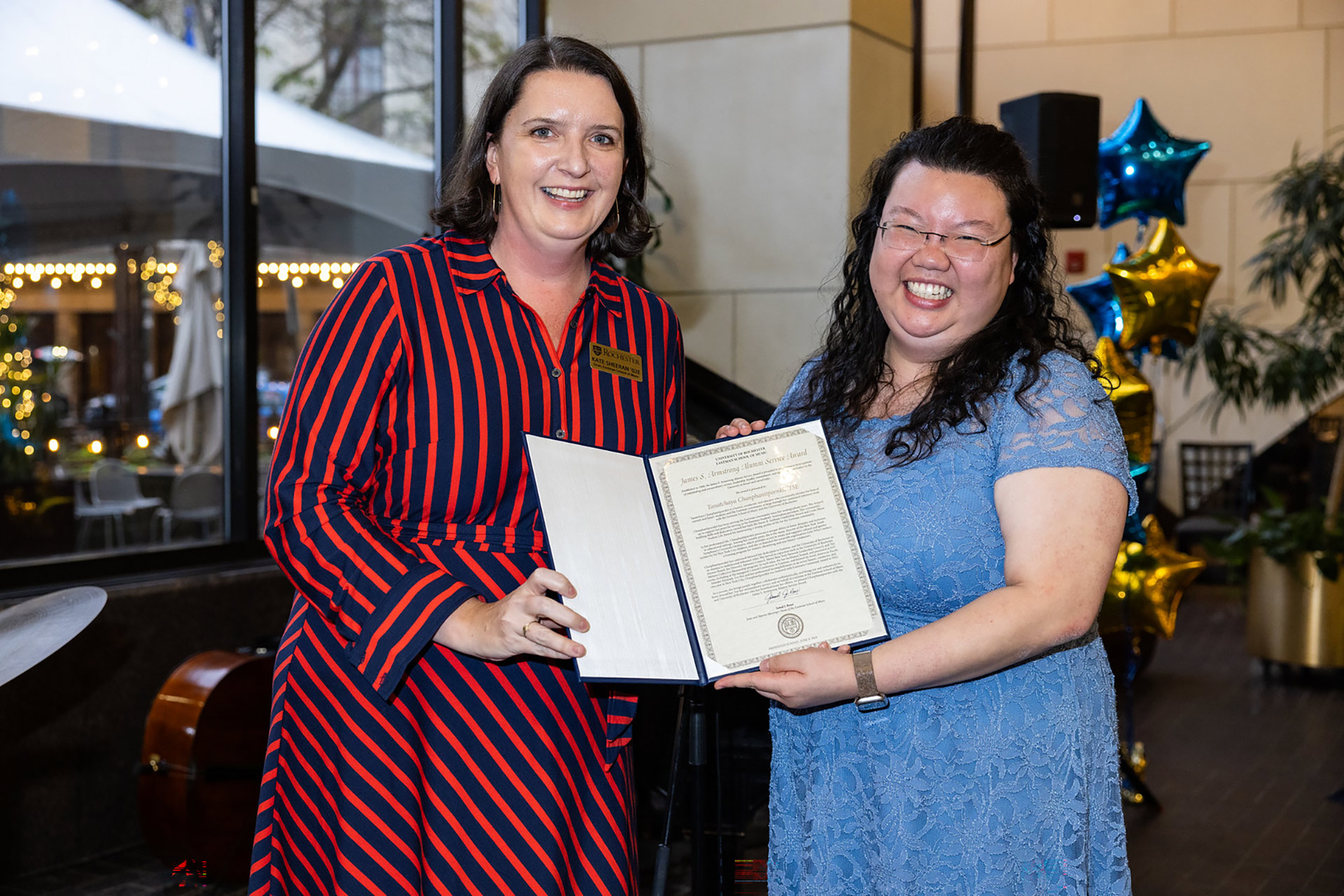 Two people pose and smile, holding an award certificate in a frame.