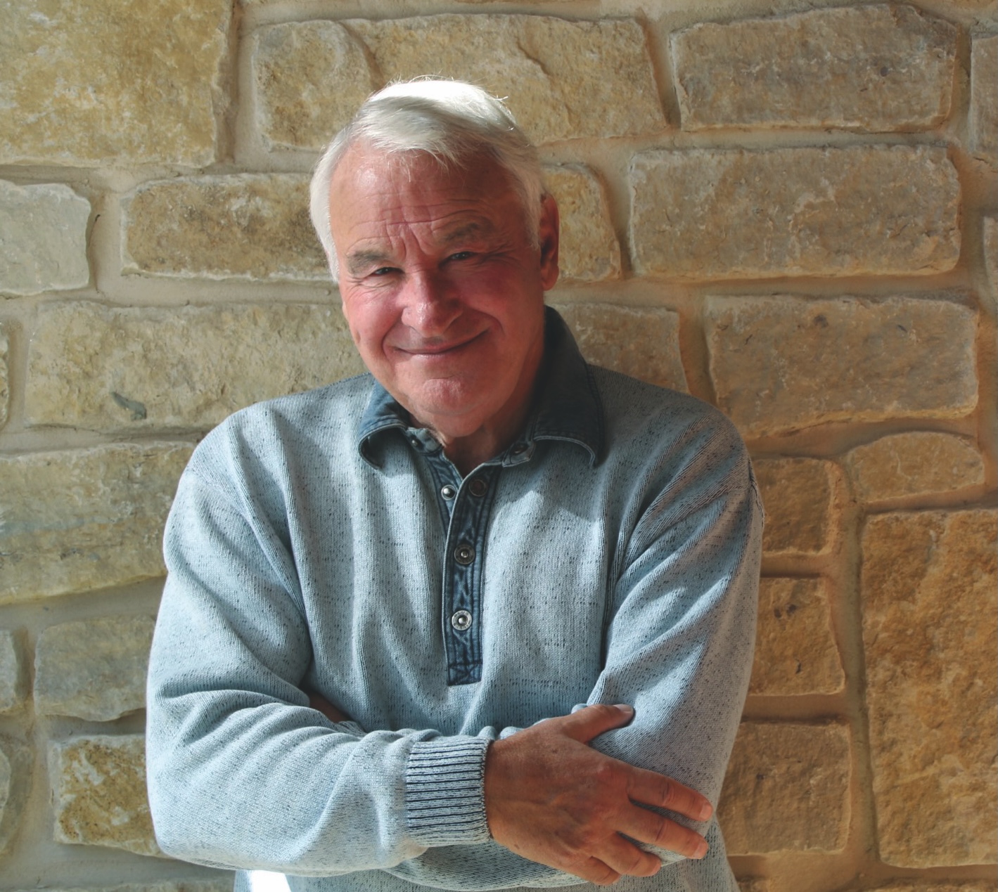 Golisano in blue shirt against tan brick wall.