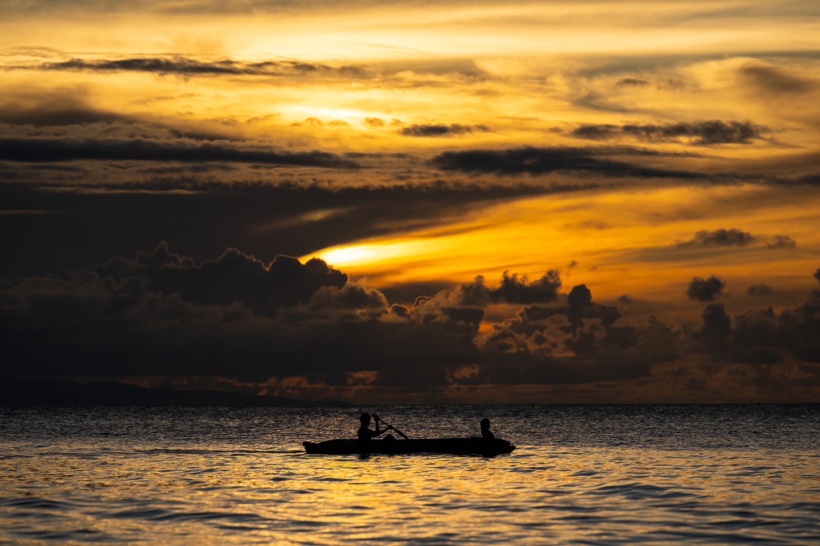 A canoe being paddled, shown in silhouette against a bright but cloudy sunrise.