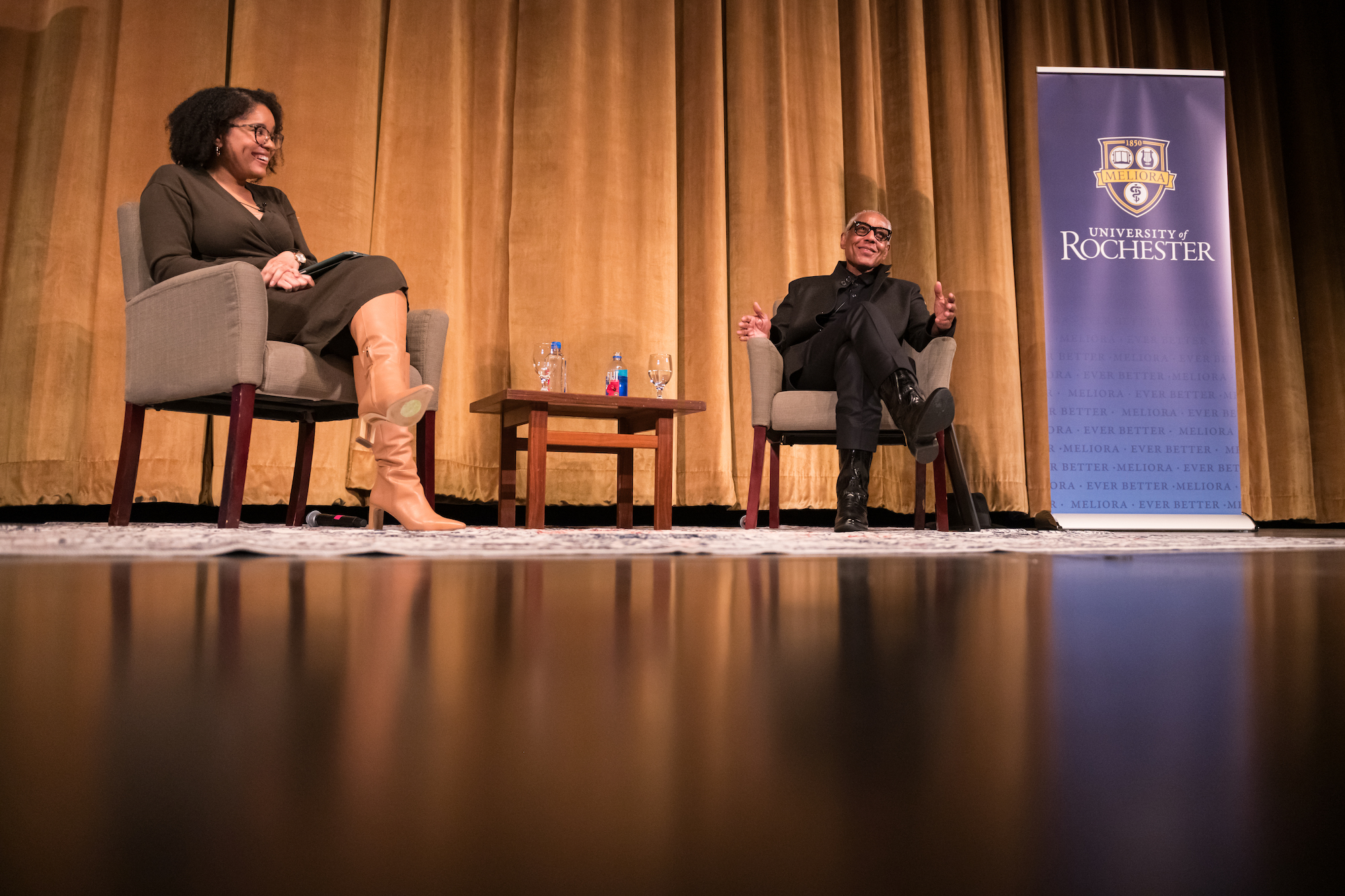 Actor Giancarlo Esposito speaks with Assistant Professor of Black Studies Jordan Ealey. They are both seated and on a stage. 
