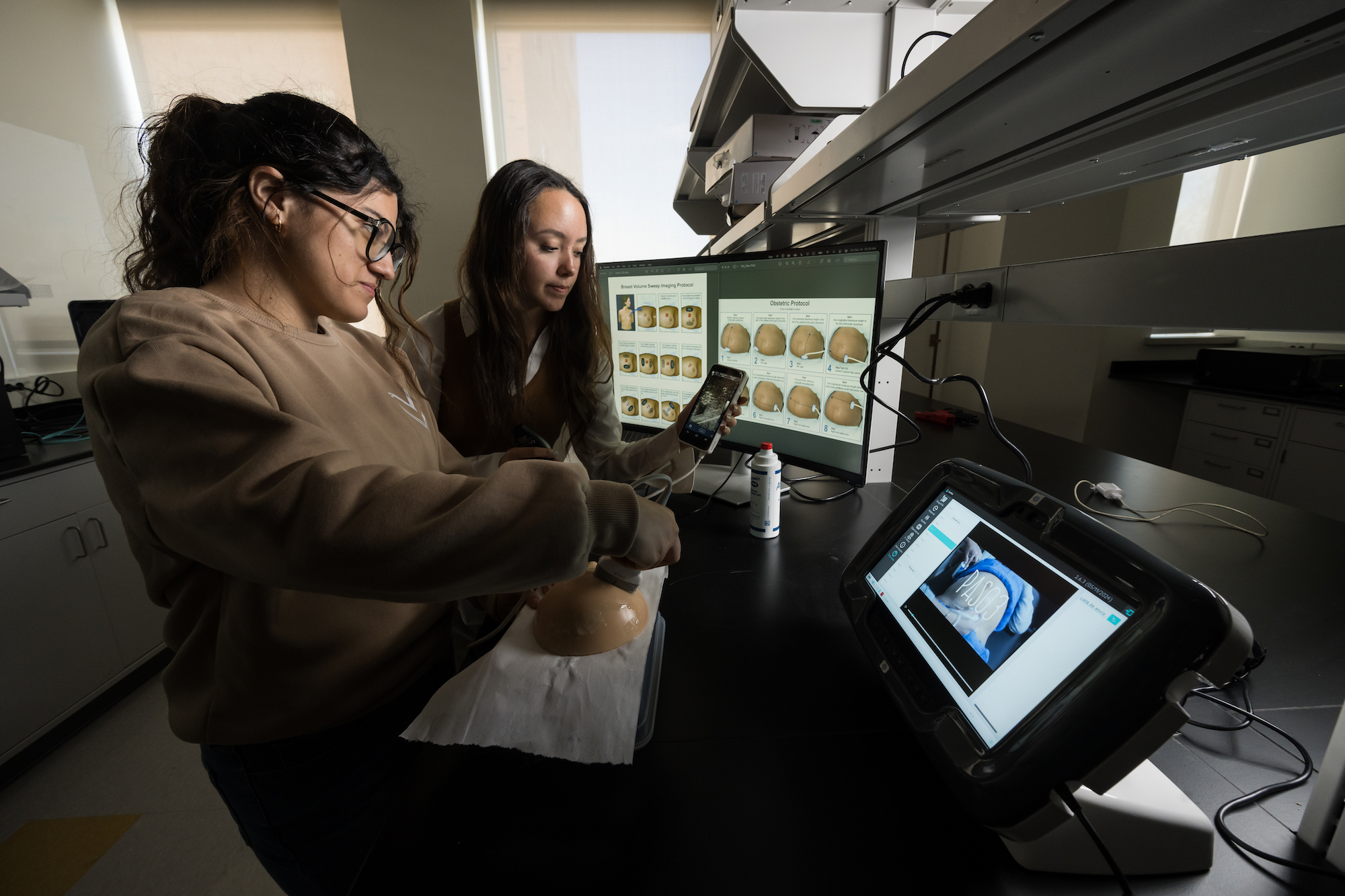 A PhD student demonstrates an ultrasound scanning protocol for breast cancer screening to an undergraduate student. 