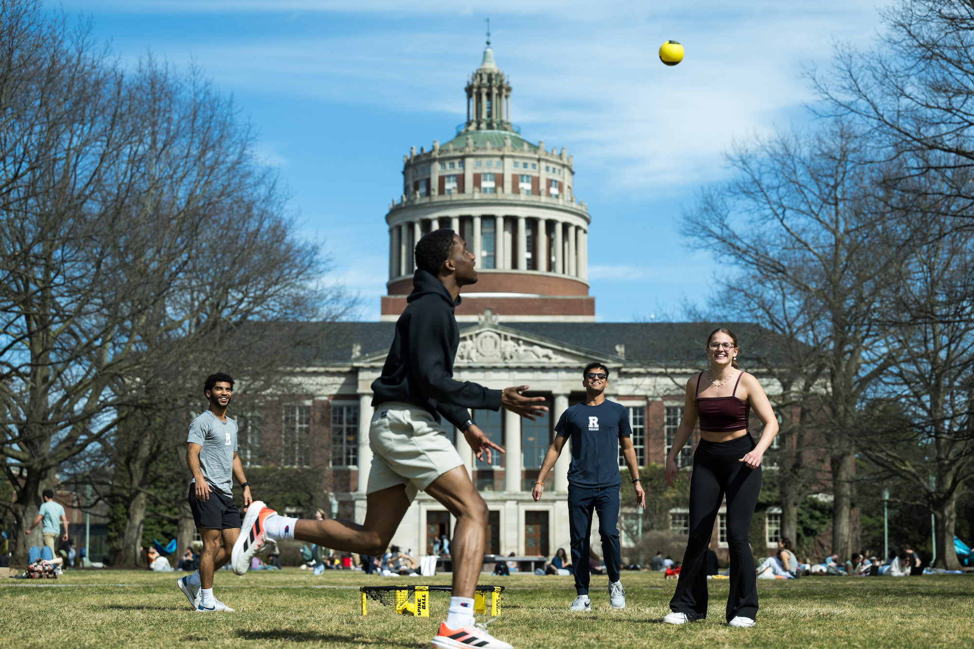 Four students play spike ball on the quad. 