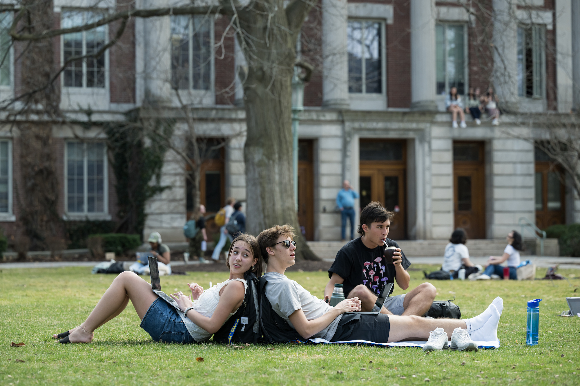 Students sit back to back on a warm afternoon on the quad. 