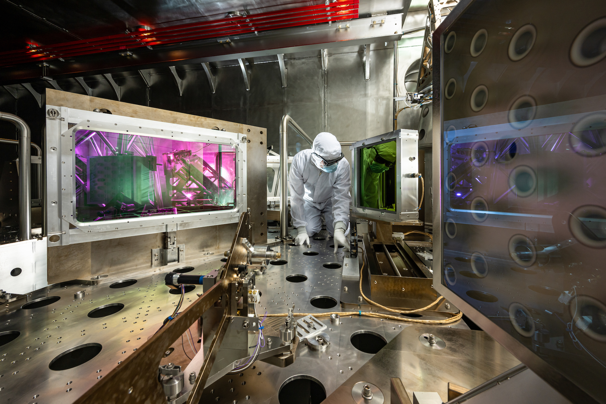 A man in a white clean suit is inside the Grating Compressor Chamber of the OMEGA EP Laser System.