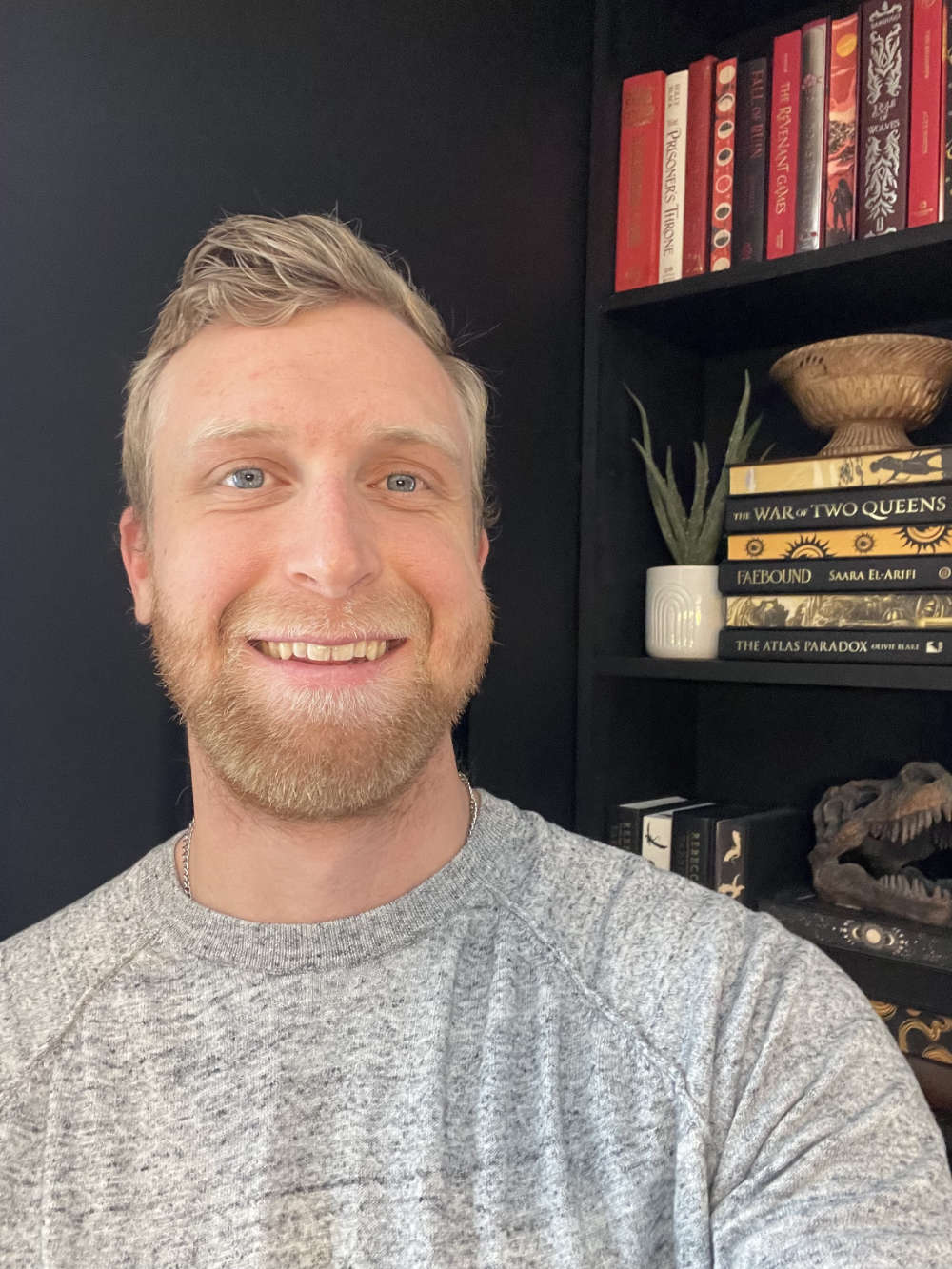 John Ghyzel smiles at the camera with a bookshelf in the background.