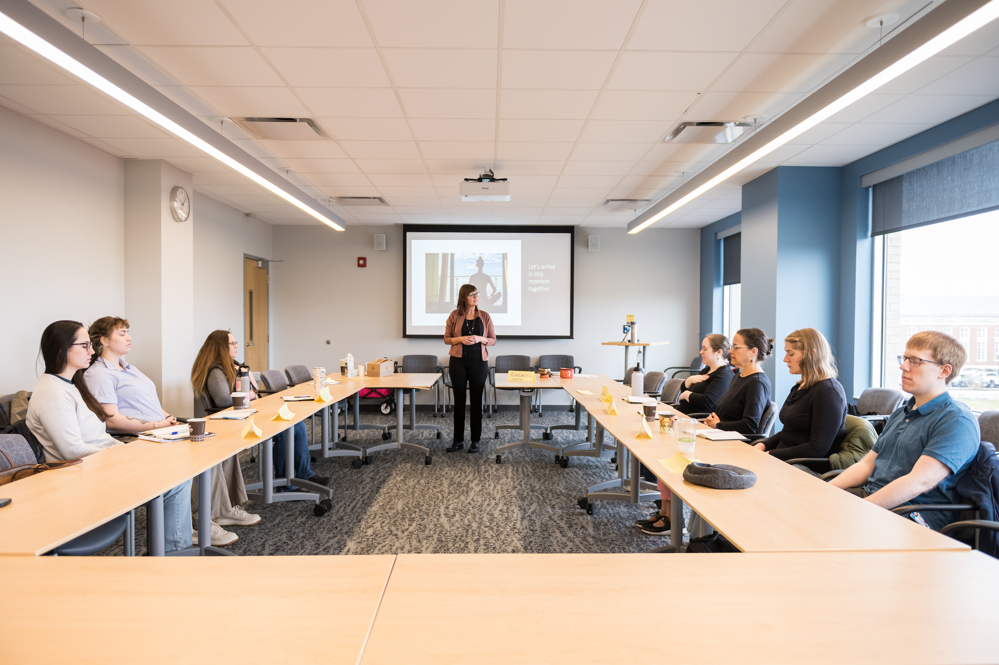 Faculty members sit around a conference room table, led in meditation. 