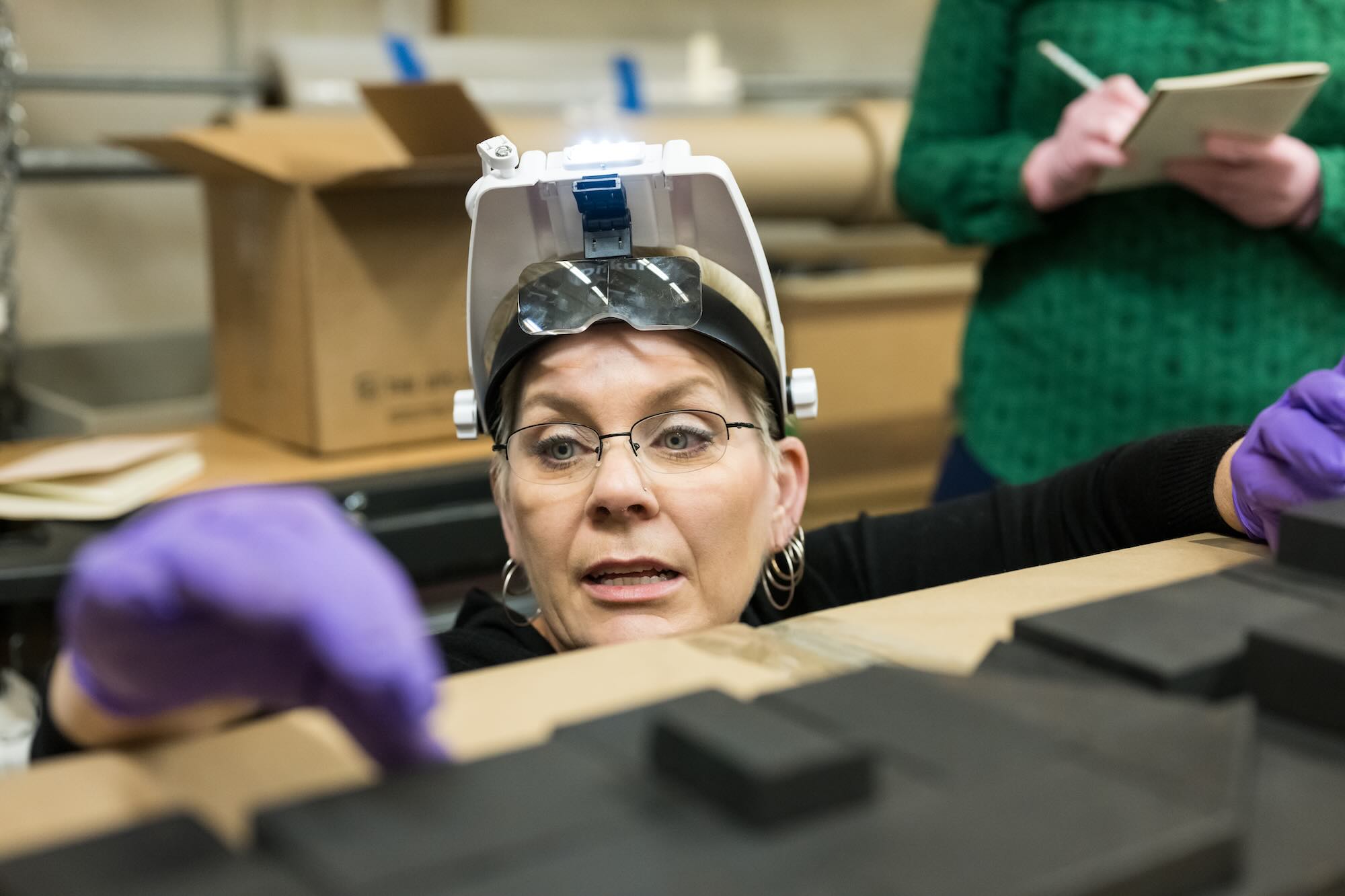 Art conservator Kasia Maroney crouches down for a closer look at a piece of art on a table.