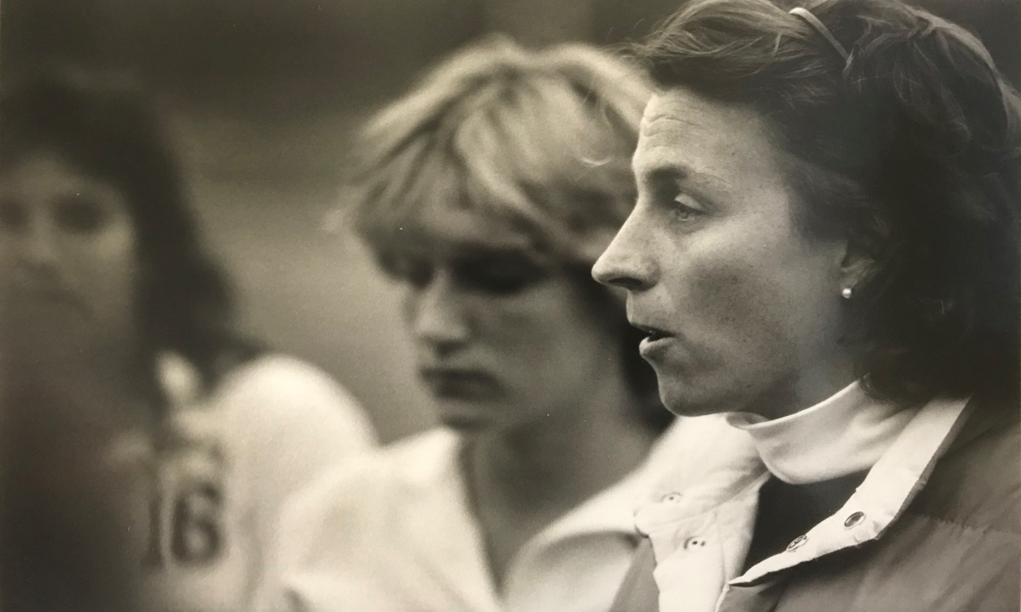 Close up of Jane Possee standing next to and coaching several female athletes.