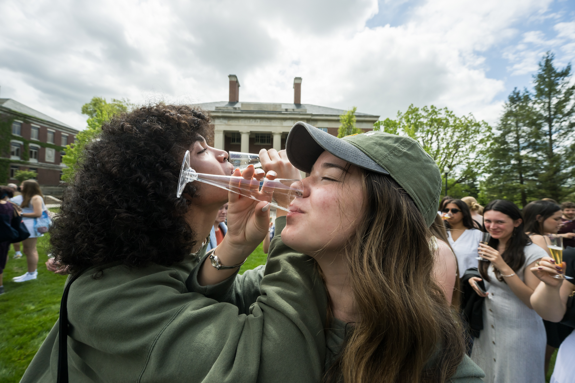 Two students, arms interlocked, share a champagne toast. 