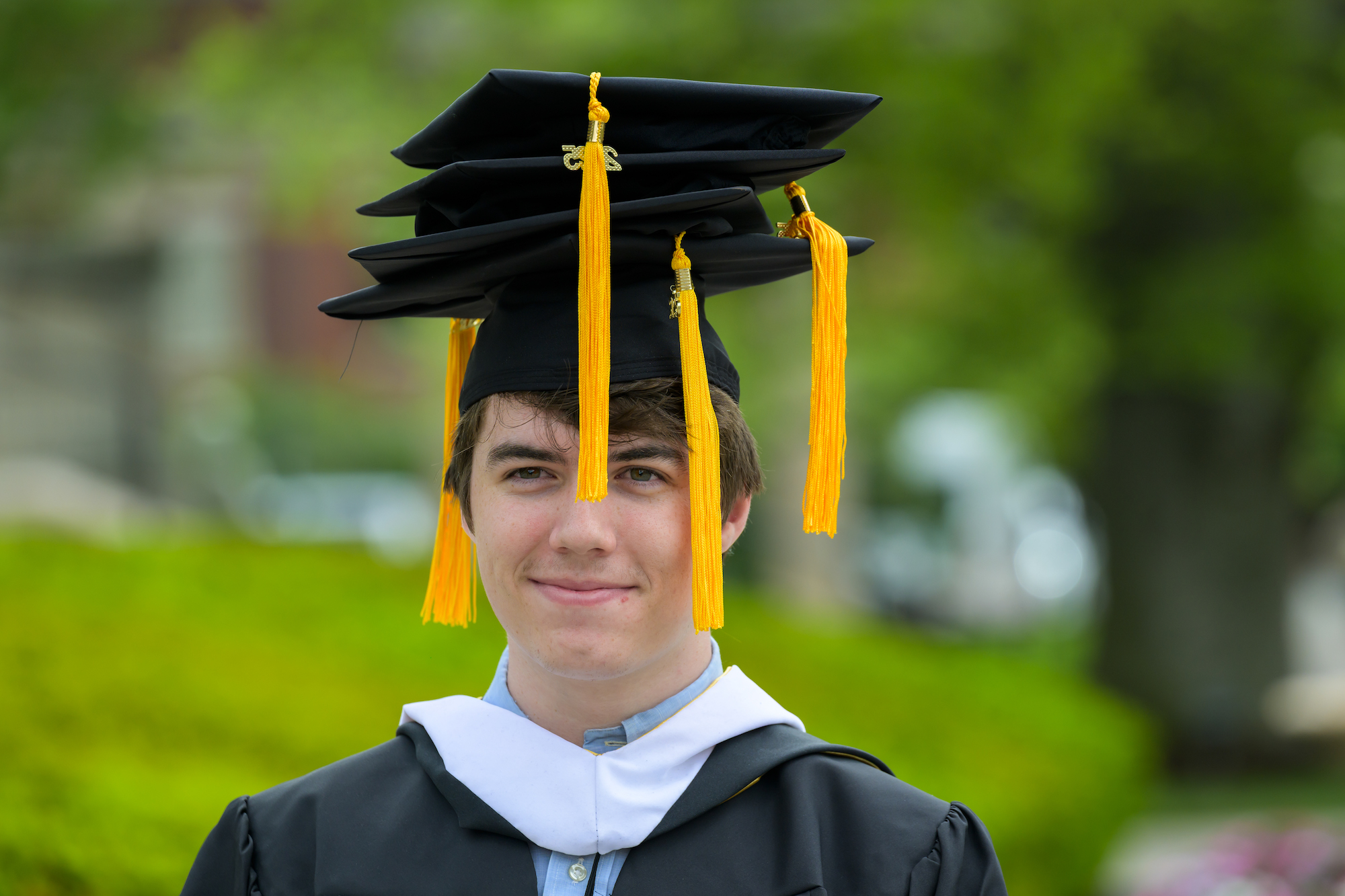 A student in graduation regalia wears four mortarboards.
