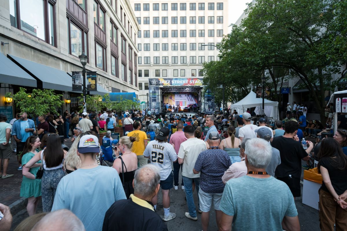 A lively crowd gathers on a street during the Rochester Jazz Fest, enjoying music and festivities.