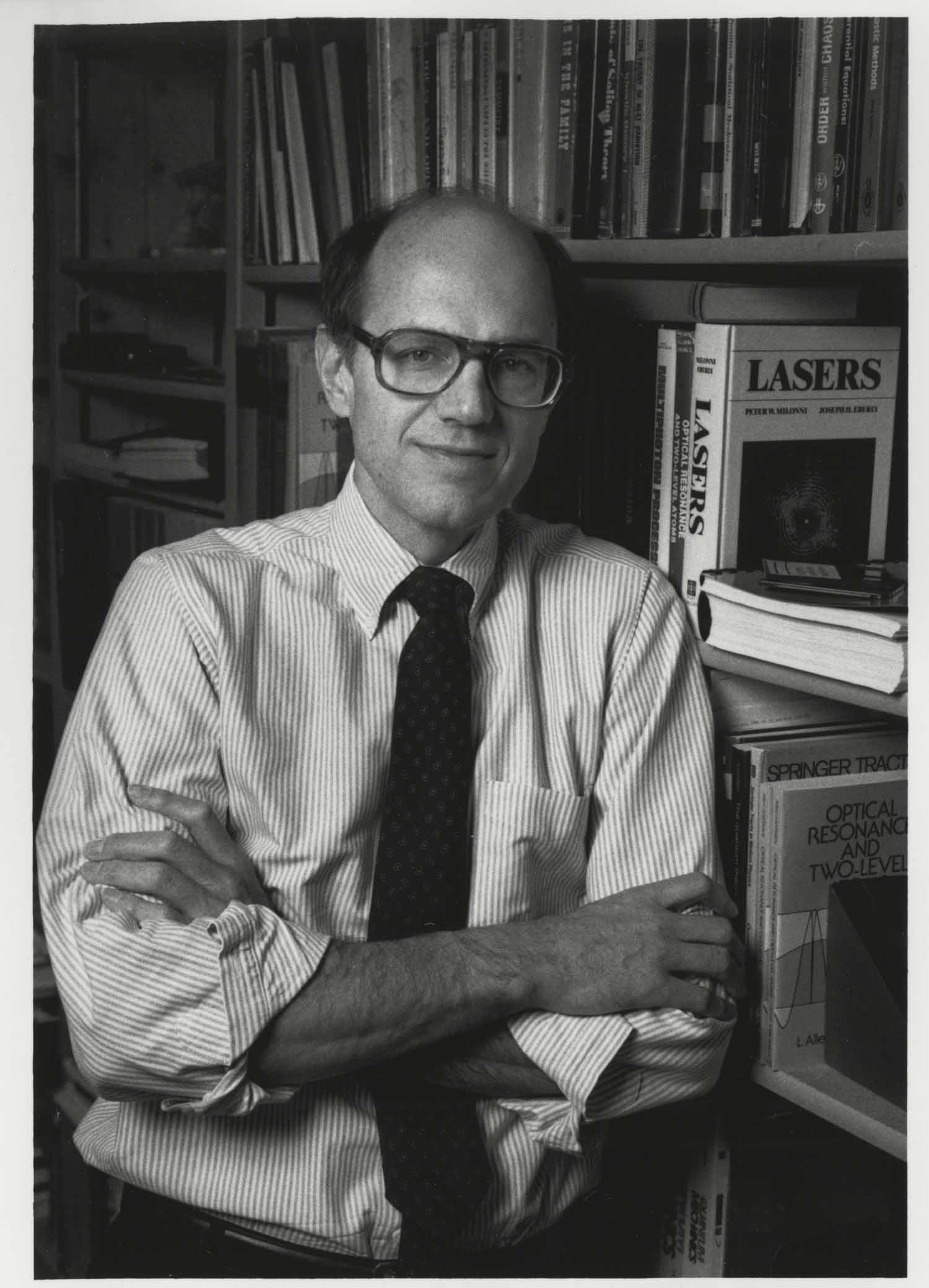 Black and white archival image of Joseph Eberly leaning against a bookshelf with a nearby textbook that says