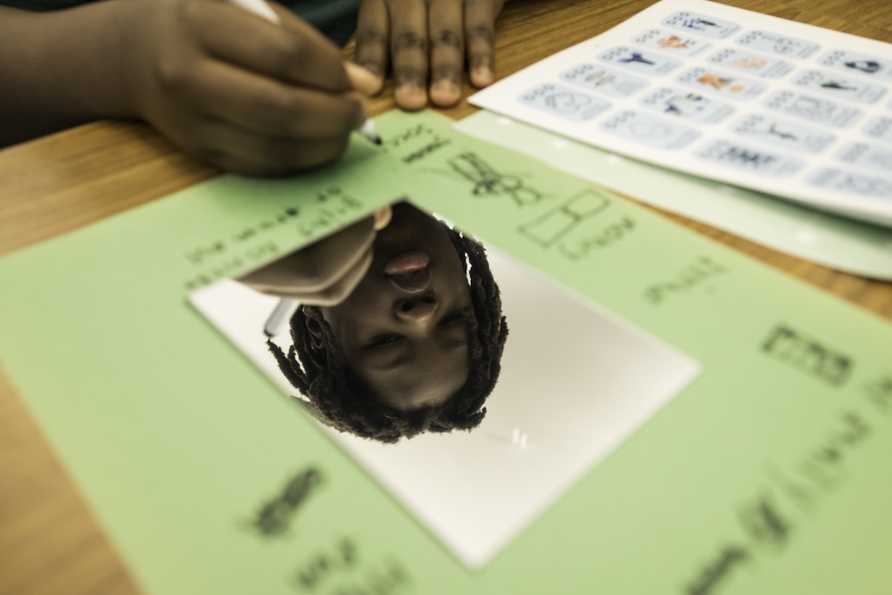 Close-up of a student’s reflection in a mirror while writing on a green worksheet during a classroom activity.