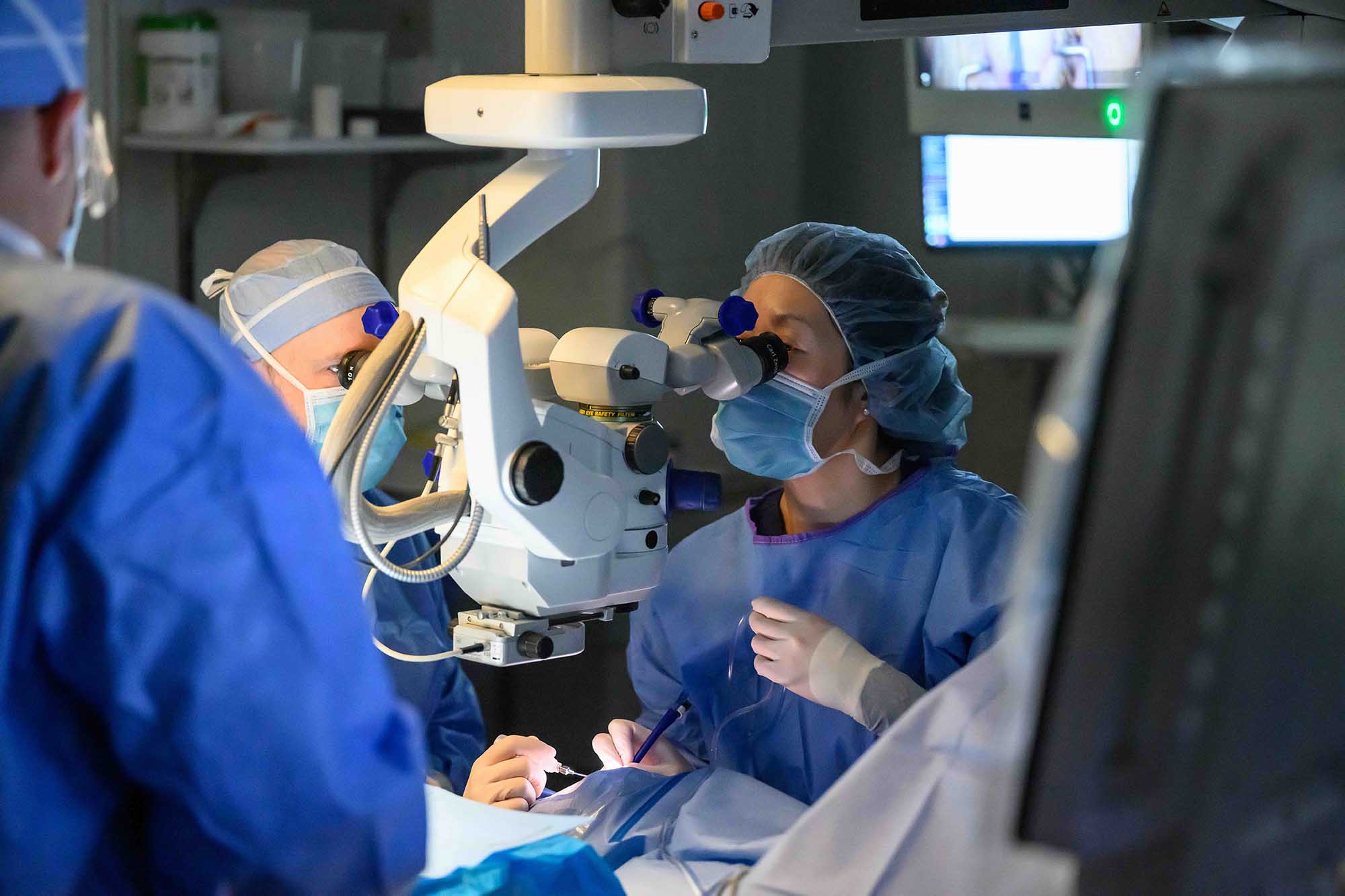 An ophthalmologist peers into a microscope while surgically implanting intraocular lenses for a patient.