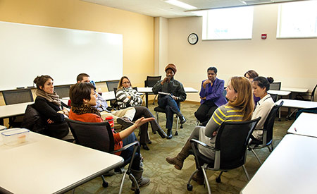 Group of graduate students sits in a classroom, in a circle of chairs. 