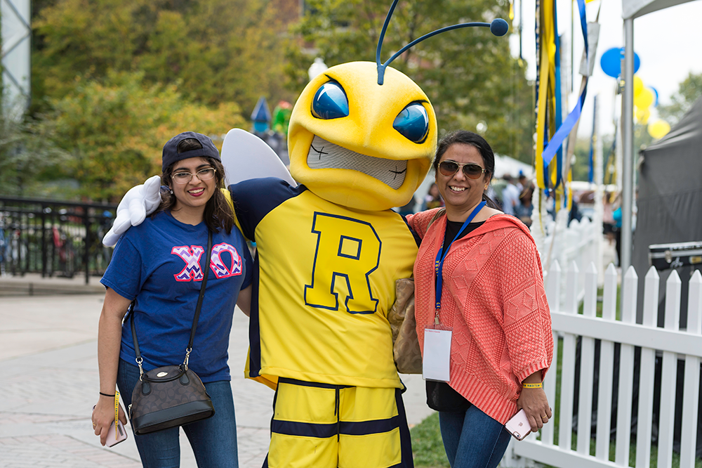 A student and their parent pose with Rocky at a previous Meliora Weekend