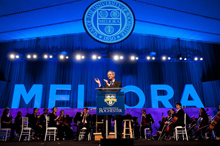 President Joel Seligman applauding at podium