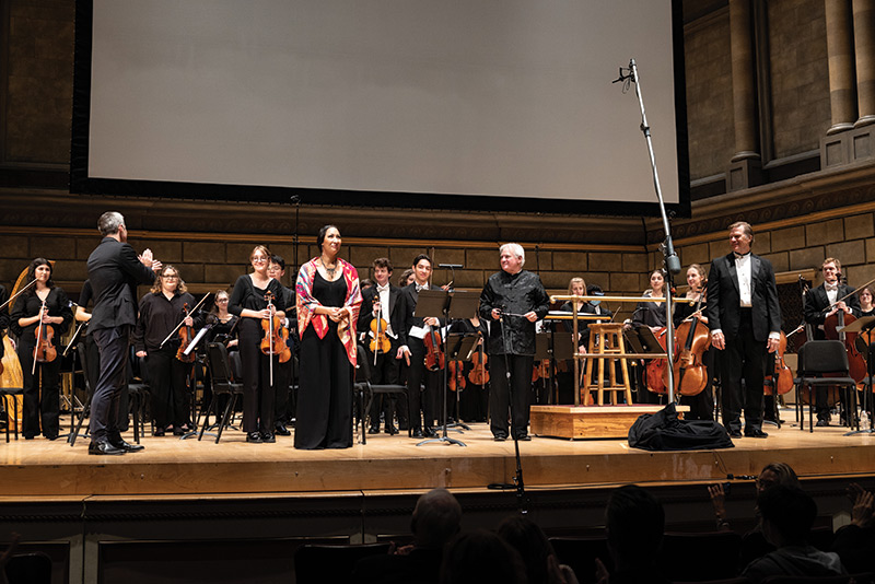 photo of University of Rochester alumni and student musicians receiving applause after a performance on a concert stage