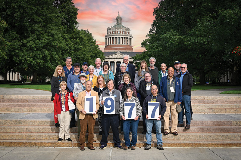 photo of University of Rochester class of 1977 standing on the steps of the quad holding signs that spell out 1-9-7-7