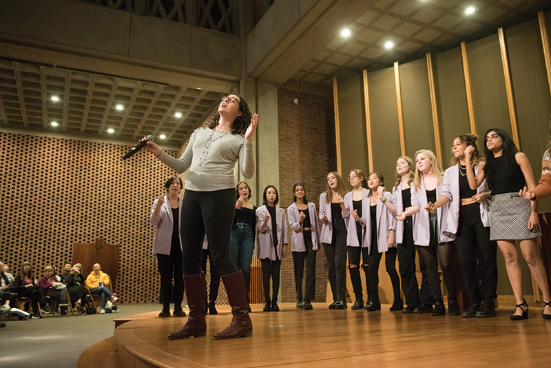 photo of University of Rochester alumna pausing during a singing performance on a campus stage with an a cappella ensemble behind her