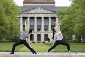 Two students doing yoga on Eastman Quad in front of Rush Rhees Library
