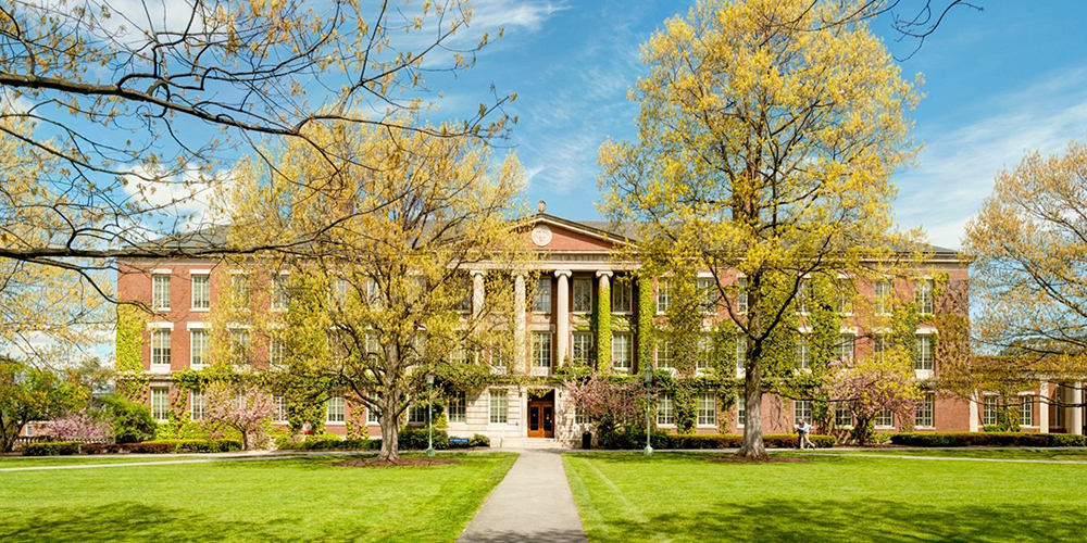 A high definition exterior view of a large brick building surrounded by trees on a sunny day.