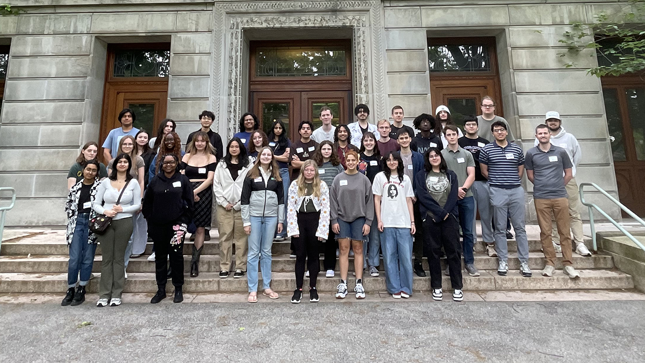 A group posing for the camera on the steps of a collegiate building.