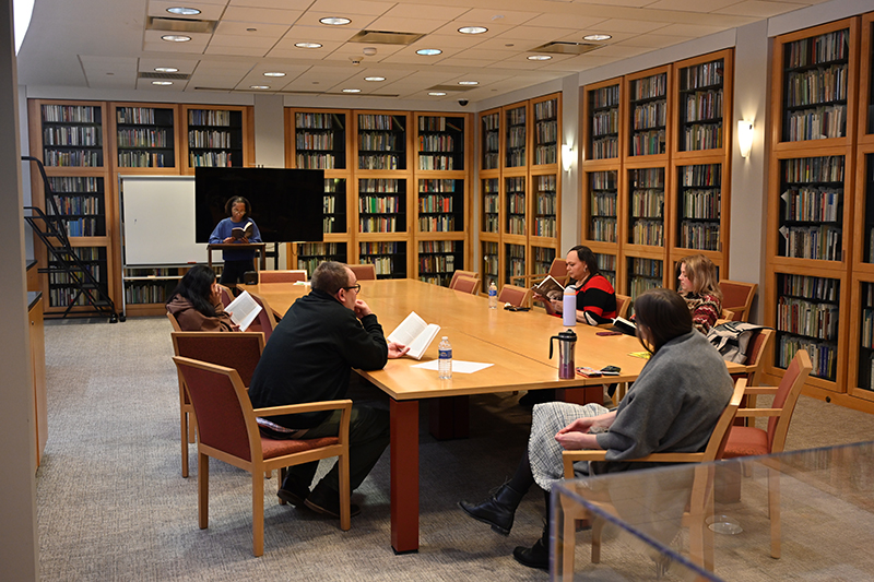A person sitting at a table in the library with bookshelves in the background.