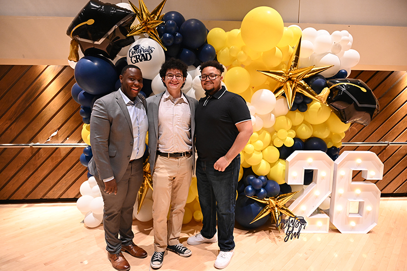 Three people pose in front of a balloon wall.