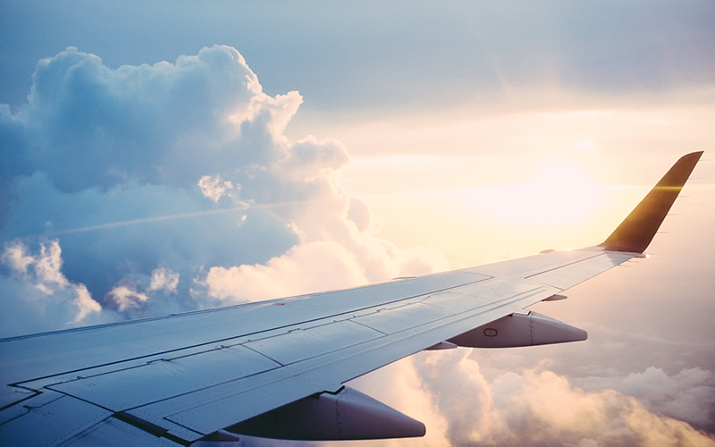 Photo of a plane wing with clouds and a shining sun in the background