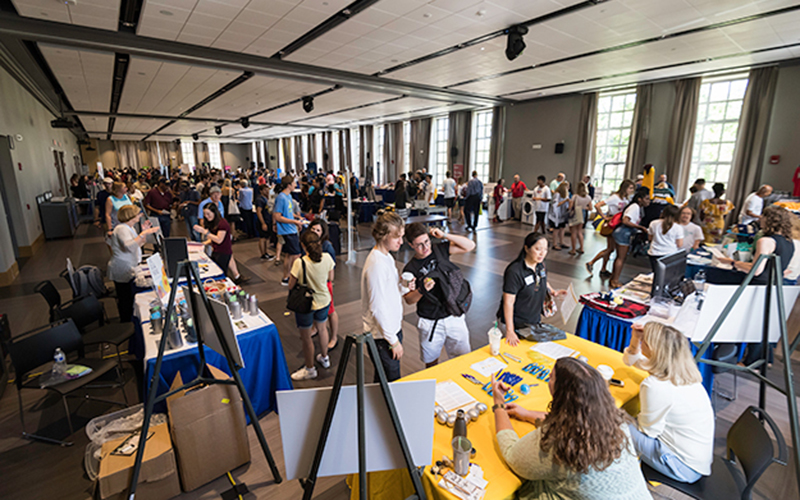 Photo of students and staff interacting at tables set up in Feldman Ballroom