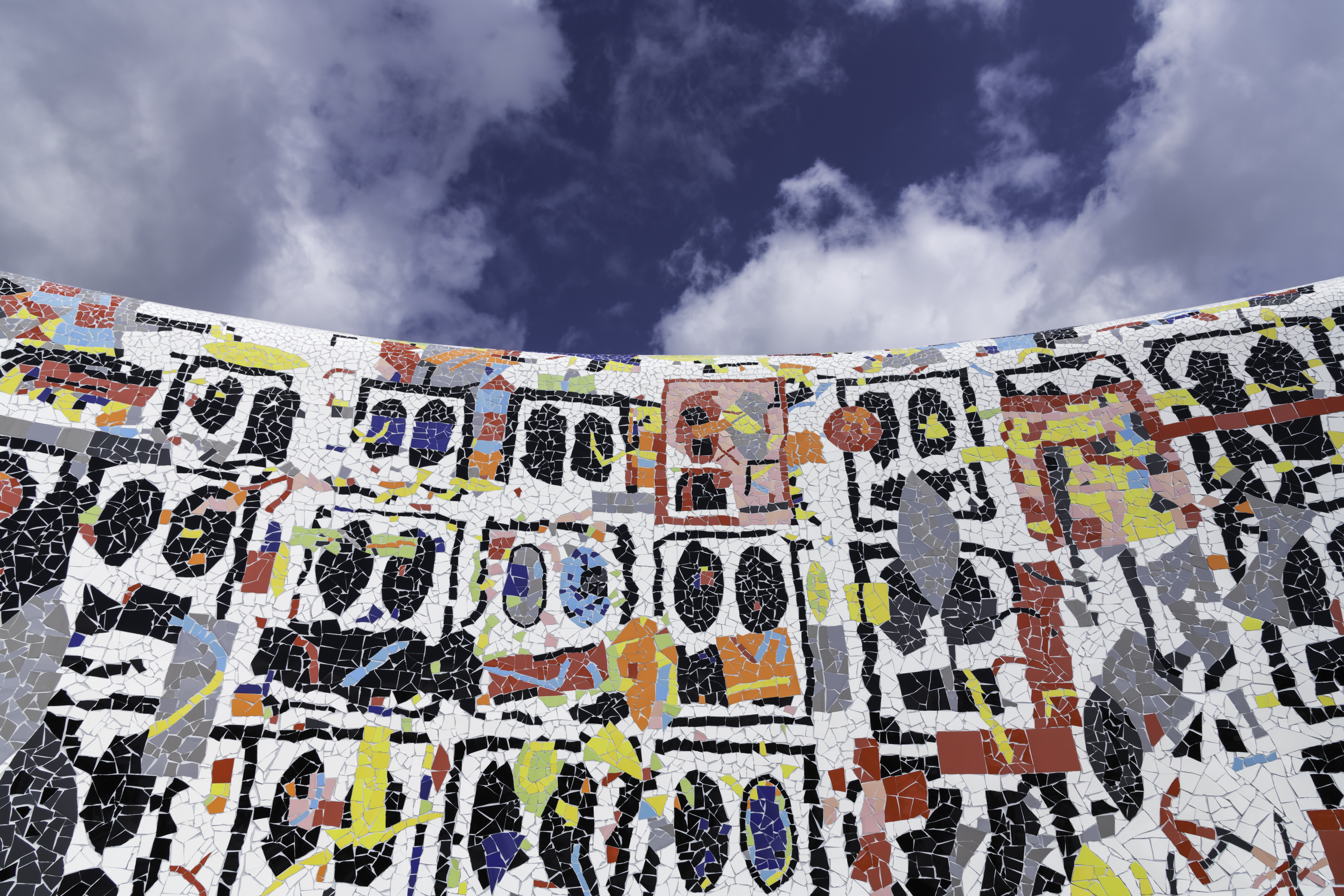 Against a blue sky with clouds, the Centennial Sculpture Park at University of Rochester's Memorial Art Gallery consists of black, neon orange, white, gray, blue, and green mosaic pieces.