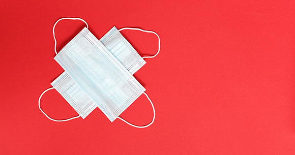 Two face masks laying on top of each other as a cross on a red background