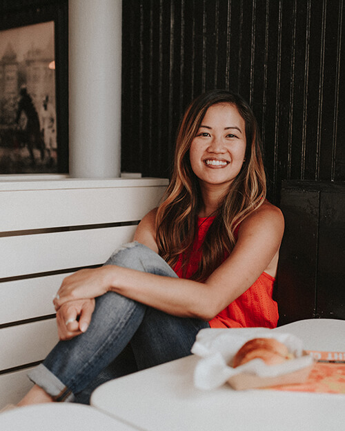 Linh Phillips ’13S (MBA) is sitting on a white bench smiling as a meal is on the table in front of her within a basket.