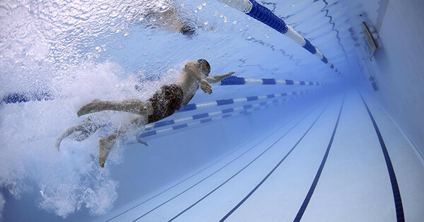 a submerged shot of three males swimming within a pool which appears to be in a active race