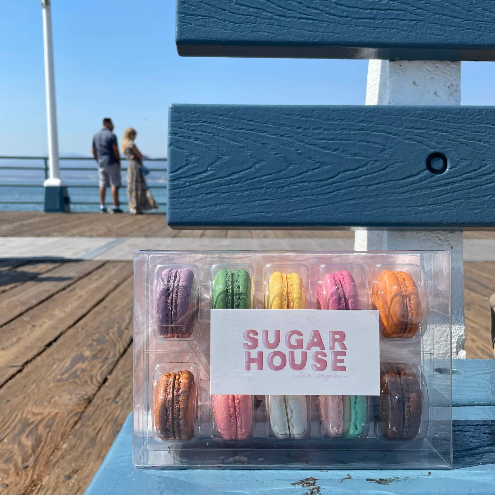 photo of a sweet house package sitting on a blue bench on a boardwalk as a couple gaze at the water in the background