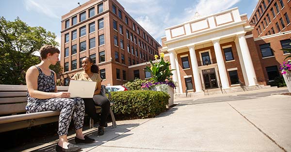 2 women on a bench talking in front of a building