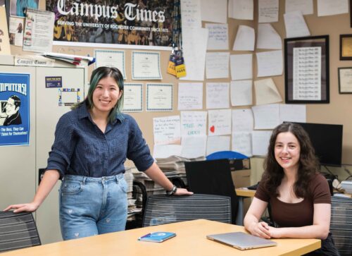2023-09-20_CT_portraits_0183 two students pose at a desk in front of The Campus Times poster and newspapers